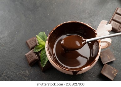 Pastry chef mixes hot chocolate with spoon in bowl, top view with mint leaves. recipe Cooking handmade chocolate bar, dessert, candies. Confectionery covered with chocolate topping with mints leaf - Shutterstock ID 2055027803