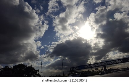 A patch of dark and white clouds stand against a blue sky over a walkover or pedestrian crossing over a busy highway. - Shutterstock ID 2115258542