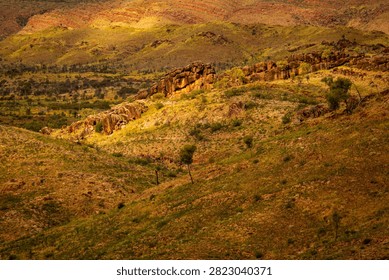 A patch of sunlight falls on an ancient natural rock wall cresting a distant hill, looking like a natural Great Wall of China, West MacDonnell National Park (Tjoritja), Northern Territory, Australia. 