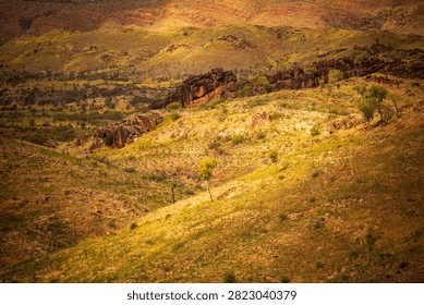 A patch of sunlight falls on an ancient natural rock wall cresting a distant hill, West MacDonnell National Park (Tjoritja), Northern Territory, Australia. 