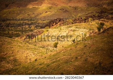 A patch of sunlight falls on an ancient natural rock wall cresting a distant hill, West MacDonnell National Park (Tjoritja), Northern Territory, Australia. 