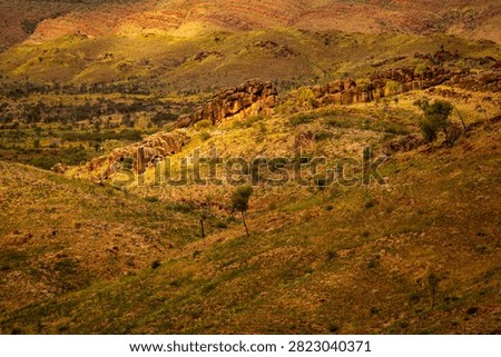 A patch of sunlight falls on an ancient natural rock wall cresting a distant hill, looking like a natural Great Wall of China, West MacDonnell National Park (Tjoritja), Northern Territory, Australia. 