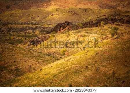 A patch of sunlight falls on an ancient natural rock wall cresting a distant hill, West MacDonnell National Park (Tjoritja), Northern Territory, Australia. 