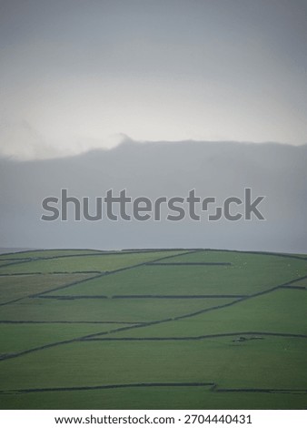 A patchwork of agriculture fields and drystone walls in the UK with a moody sky