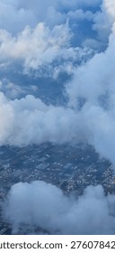 Patchwork fields and buildings appear below broken cloud layers in a high altitude view.