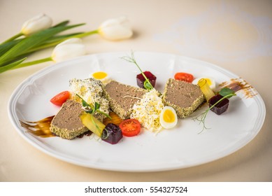 Pate with jelly and vegetables. Appetizer close-up in white plate on a table with flowers.