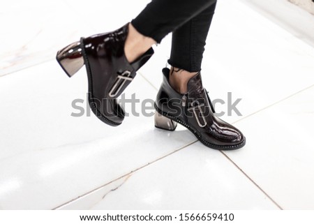 Patent black stylish fall boots with silver heel on female legs. Close-up of fashionable autumn-spring women shoes. New collection. Casual youth fashion.