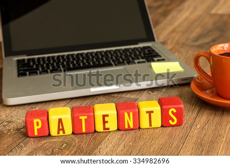 Patents written on a wooden cube in front of a laptop