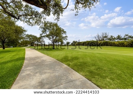 path in a beautiful and large park within the country club in coral gables, large spaces, trees, tropical vegetation, palms, blue sky

