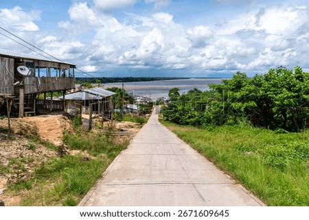A path leads down into a rural settlement on the bank of the Amazon River in Peru under a cloudy sky