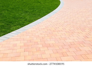 A path made of bricks gently curves beside an area of green grass in a recreational space. This setting offers a view of natural elements and man-made structures.
