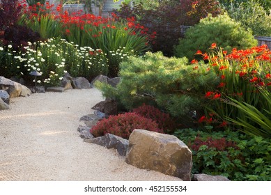 A Path Made Of Course Sand Winds Through A Perennial Garden In The Late Afternoon Sun.