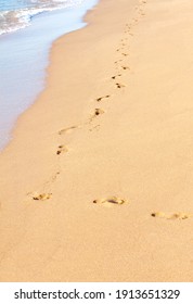 A path made of footprints of bare human feet goes along the yellow sand of the coast along the sea