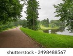 A path in a park with a river and trees. The path is wet from the rain