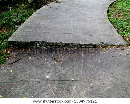 The path of the pedestal is damaged by the roots of the tree below which grows to cause the cement path to be uneven.