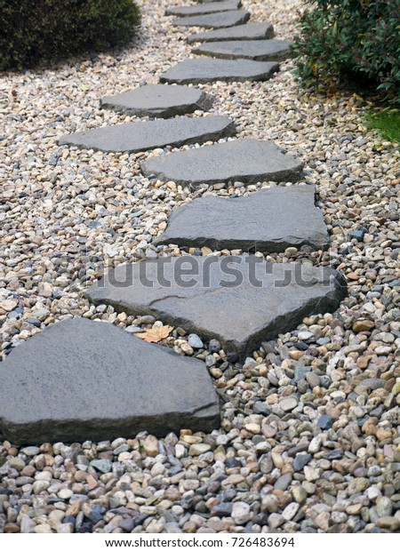 Path of plated stones on gravel bed in Japanese\
Garden. Meditative stone walkway. Garden architecture, pathway\
accessory to garden pond.