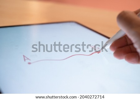 The path from point A to point B, the concept of achieving a goal or moving along a given trajectory. The hand draws on the tablet screen using a stylus. close-up small depth of field