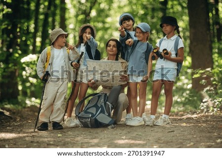 Path searching, sitting and reading a map. Woman is doing tour for group of kids in the forest.