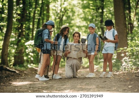 Path searching, sitting and reading a map. Woman is doing tour for group of kids in the forest.