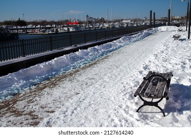 The path in the snow and the bench on the Morris Channel Basin Walkaway in Jersey City in a sunny winter day - Shutterstock ID 2127614240