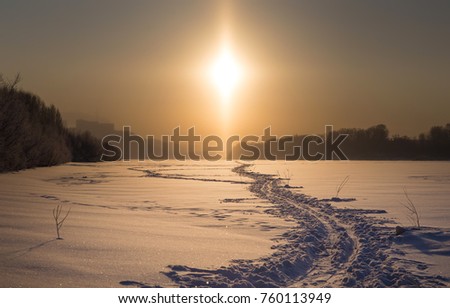 a path in the snow retreating into the distance against the background of the winter landscape and the natural phenomenon of the parhelion or halo.