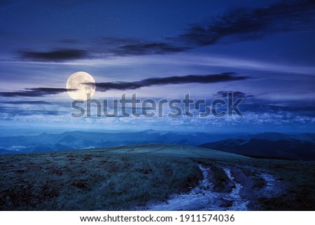 path through green grassy mountain meadow at night. beautiful summer landscape in full moon light. fine weather with fluffy clouds on the blue sky