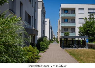Path through a modern building area features well-kept gardens and parking for bikes on a sunny day.
