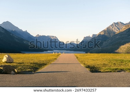 Path to tranquil lake framed by majestic mountains under a clear, blue sky. Waterton, AB