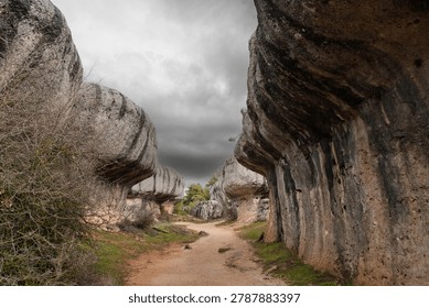Path winding through the unique and eroded limestone rock formations creating mushroom like shapes and a surreal landscape under a cloudy sky in Ciudad Encantada, Cuenca