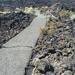 A Path Winds Through The Lava Rock Fields And Bushes That Somehow Grow There At Lava Butte In Central Oregon On A Summer Day.