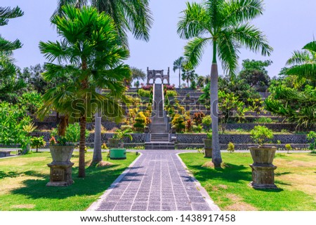 A pathway leading to the stairs of a palace in the garden at Ujung Water Palace (also known as Ujung Park or Sukasada Park) with tropical trees, manicured lawns and ornamental pots in Bali, Indonesia