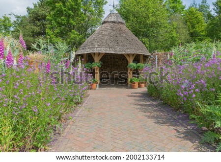 Pathway through the plant filled borders leading down to the rest area with the conical thatched roof