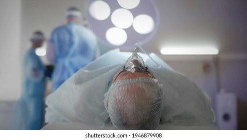 Patient With Anesthesia Mask Lying On Operating Table With Doctors Preparing For Surgery. Surgeons In Operation Room Making Preparation. Healthcare And Medicine Concept