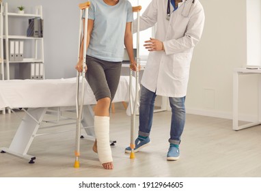 Patient with broken leg assisted by doctor. Injured young woman stands up from examination bed at hospital and walks using crutches with help of medical specialist. Rehabilitation after injury concept - Powered by Shutterstock