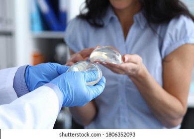 Patient Of Clinic Hold Breast Implant In His Hand And Touch It With Her Finger. Doctor Hold Silicone Material In His Hand And Show Woman.