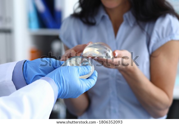 Patient of clinic hold breast implant in his hand
and touch it with her finger. Doctor hold silicone material in his
hand and show woman.
