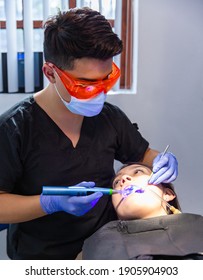 Patient In A Dentist Office Receiving A Tooth Whitening Procedure. Dentist Has PPE With Face Mask, Gloves And Protective Glasses.