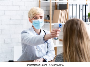 Patient examination. Woman doctor in protective mask measures temperature with contactless thermometer in interior of office - Shutterstock ID 1733407046