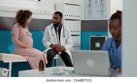 Patient expecting child meeting with physician in medical cabinet, attending exam appointment to receive pregnancy advice. Pregnant woman talking to male doctor about childbirth. - Powered by Shutterstock