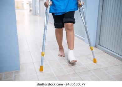 Patient with injured ankle sprain from accident, using walking stick crutches to self balance and walk. Medical healthcare physical therapist hospital corridor background. - Powered by Shutterstock