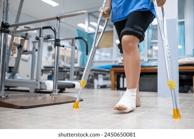 Patient with injured ankle sprain from accident, using walking stick crutches to self balance and walk. Medical healthcare physical therapist hospital corridor background. - Powered by Shutterstock