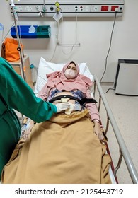 Patient Laying On Bed Receiving Medical Treatment From Nurse With Green Uniform In Intensive Care Unit Room At Hospital.