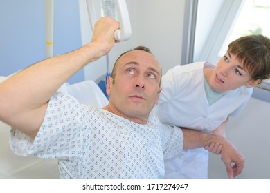 Patient Lifting Himself Out Of Bed With Hoist, Nurse Helping