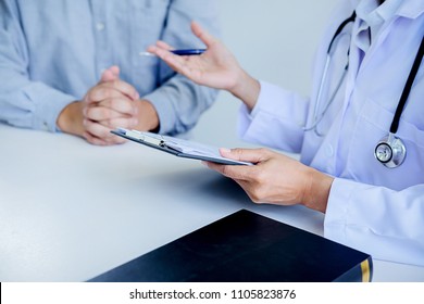 Patient Listening Intently To A Male Doctor Explaining Patient Symptoms Or Asking A Question As They Discuss Paperwork Together In A Consultation