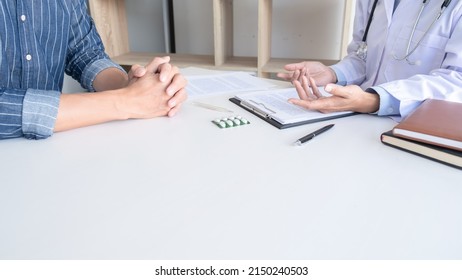 Patient Listening Intently To A Male Doctor Explaining Patient Symptoms Or Asking A Question As They Discuss Paperwork Together In A Consultation