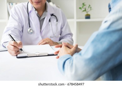 Patient Listening Intently To A Male Doctor Explaining Patient Symptoms Or Asking A Question As They Discuss Paperwork Together In A Consultation.