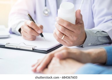 Patient Listening Intently To A Male Doctor Explaining Patient Symptoms Or Asking A Question As They Discuss Paperwork Together In A Consultation.