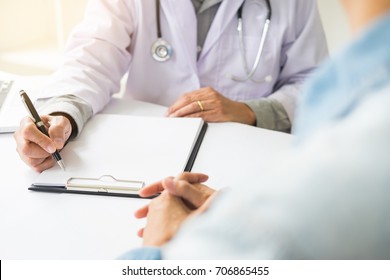 Patient Listening Intently To A Male Doctor Explaining Patient Symptoms Or Asking A Question As They Discuss Paperwork Together In A Consultation.