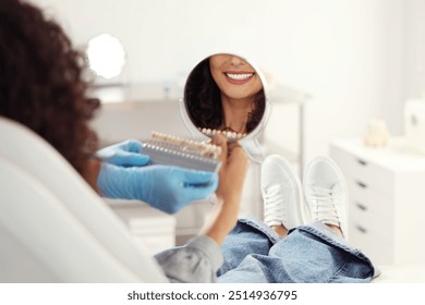 Patient looking in mirror while doctor holding teeth color chart in clinic, closeup. Dental veneers - Powered by Shutterstock