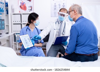 Patient looking at radiography of his skeleton during consultation with doctor in hospital wearing protection against covid-19. Medical examination for infections, disease and diagnosis. - Shutterstock ID 1826254844